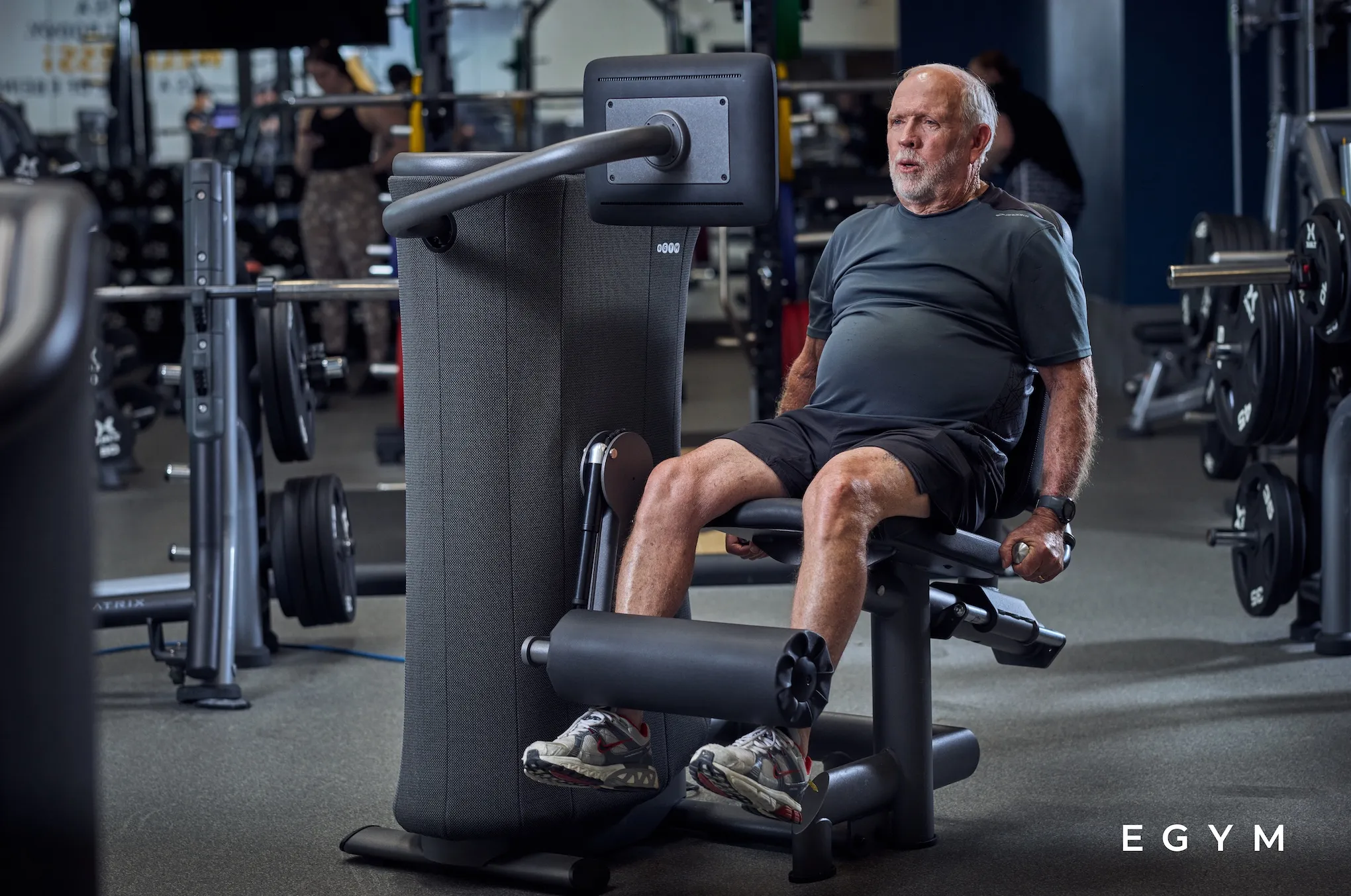 EGYM branded image of an elderly white man using one of the egym equipment machines to work out his legs.